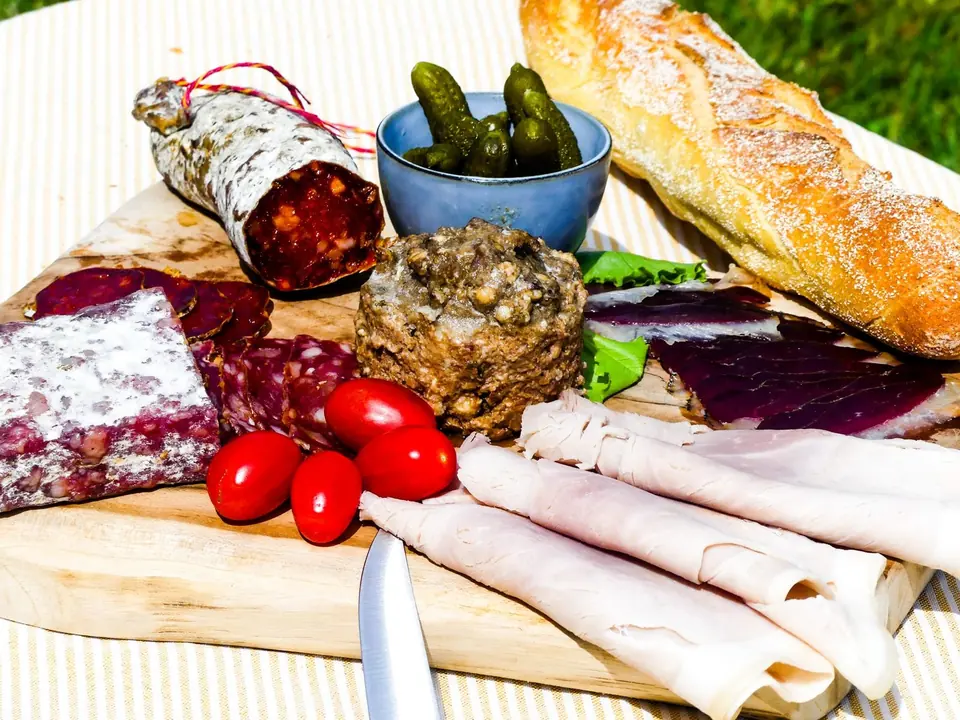 Planche de charcuterie, cornichons et baguette sur l'herbe